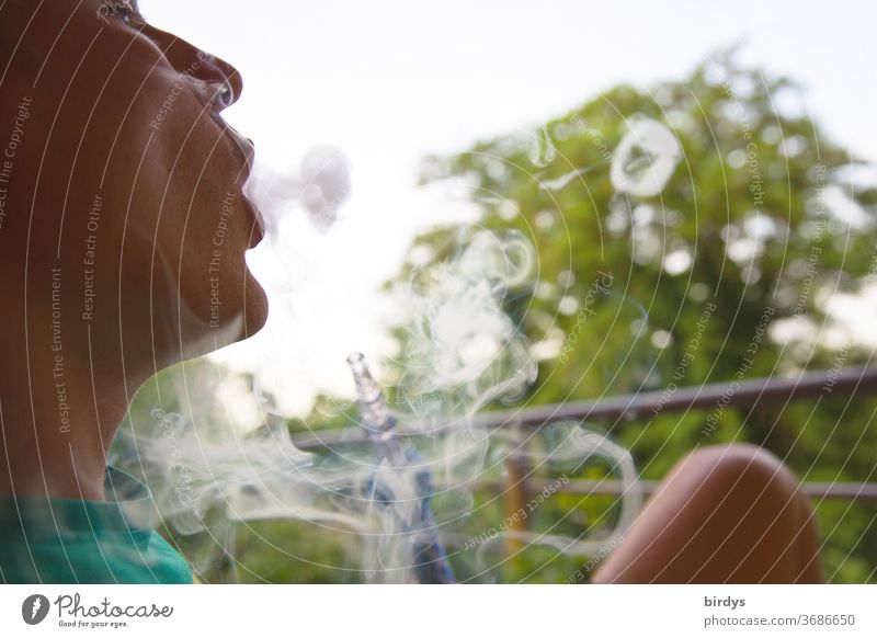 Youth smokes Shisha in the open air and blows smoke rings into the air Smoking shisha Smoke Rings of smoke younger Hookah free time Health hazard
