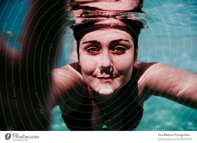 portrait of young woman diving underwater in a pool. summer and fun lifestyle touching hand swimming bubbles caucasian dive clear health light action wet