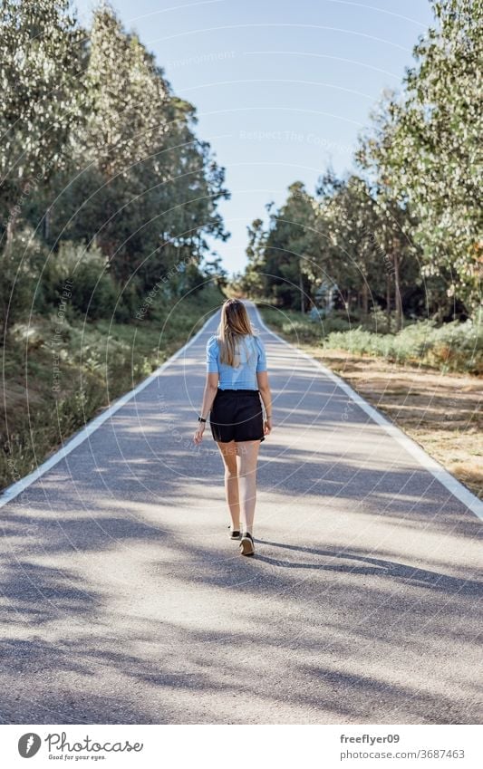 Young caucasian woman walking by an empty road near a forest lifestyle copy space countryside fashion model young blonde sunlight exterior outdoors tranquil