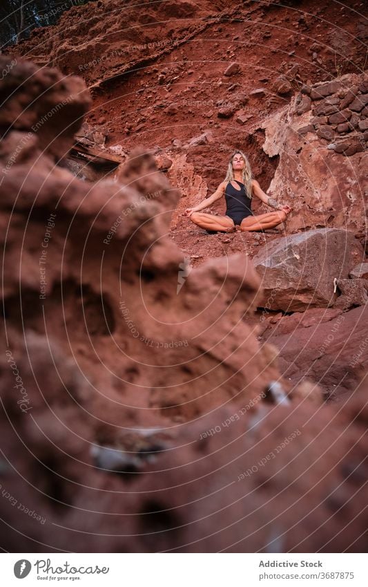 Woman in a swimsuit sitting in meditation in an arid terrain across vertical remain ruins surface isolated abandoned yoga nature fitness meditating relaxation