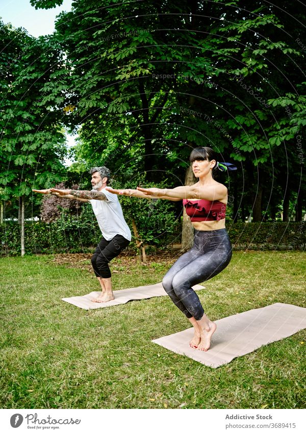 Focused couple doing yoga in Awkward pose in park awkward pose balance asana posture utkatasana together mat green garden healthy practice barefoot harmony