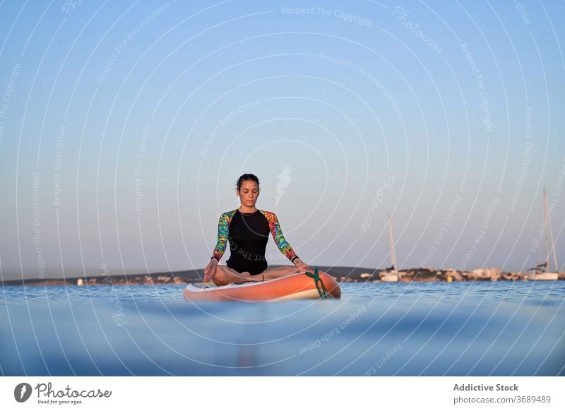 Flexible woman doing yoga in lotus pose on paddleboard sunset surfer balance sea female water healthy nature harmony relax tranquil serene closed eyes sky calm