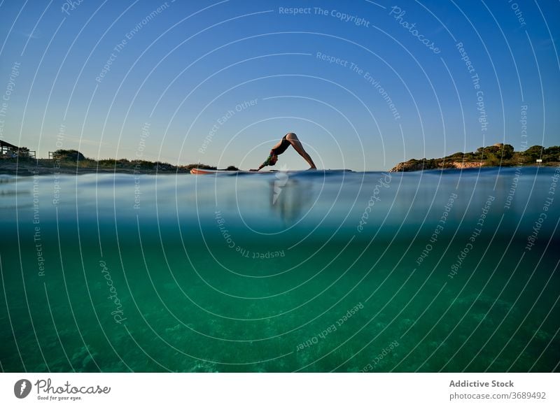 Flexible woman doing yoga on paddleboard sunset pose surfer Adho Mukha Svanasana balance sea female water healthy nature harmony relax tranquil serene sky calm