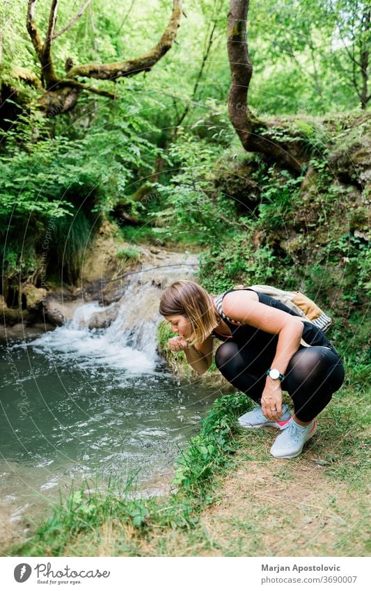 Young female nature explorer drinking water from the spring active activity adult adventure backpack backpacker creek ecology exploring forest freedom freshness