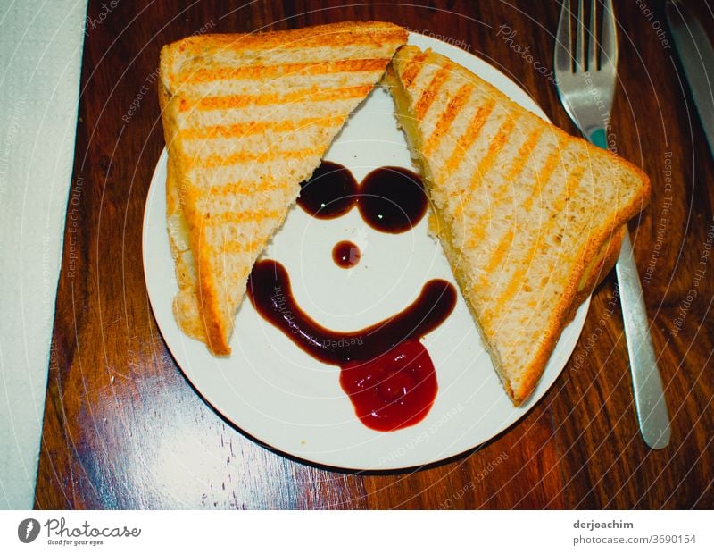 Breakfast Smiley, A shared bread on the plate. With ketchup a smiley face. On the right a fork on a wooden table. breakfast snack Food Colour photo Delicious