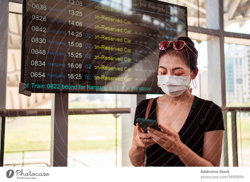Asian woman using smartphone at bus station schedule timetable mask coronavirus wait female ethnic asian digital covid focus outbreak epidemic protect