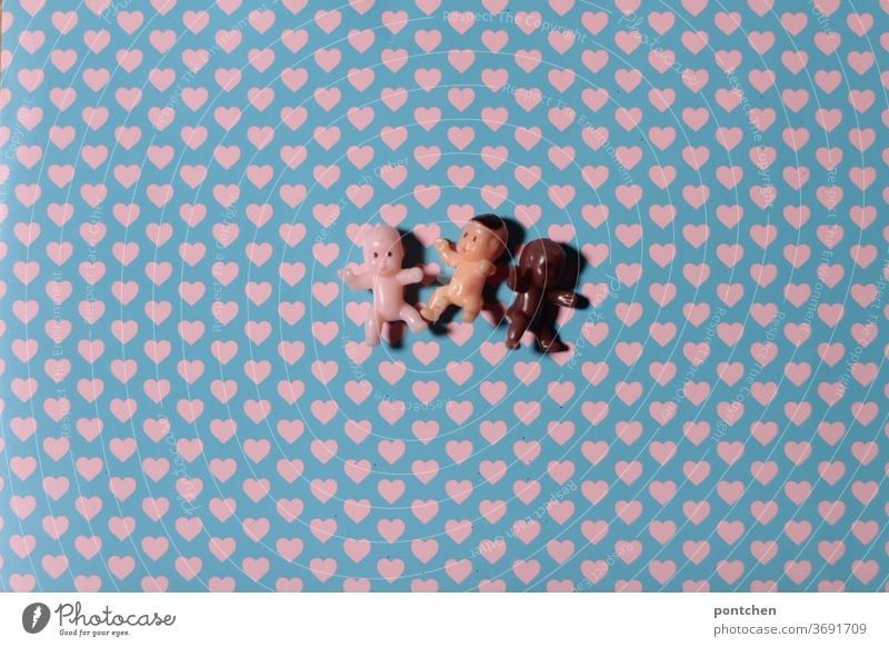 Three little baby dolls with different skin colours lie on a background with hearts. Love, tolerance, humanity, diversity Babies Skin color PoC People of color