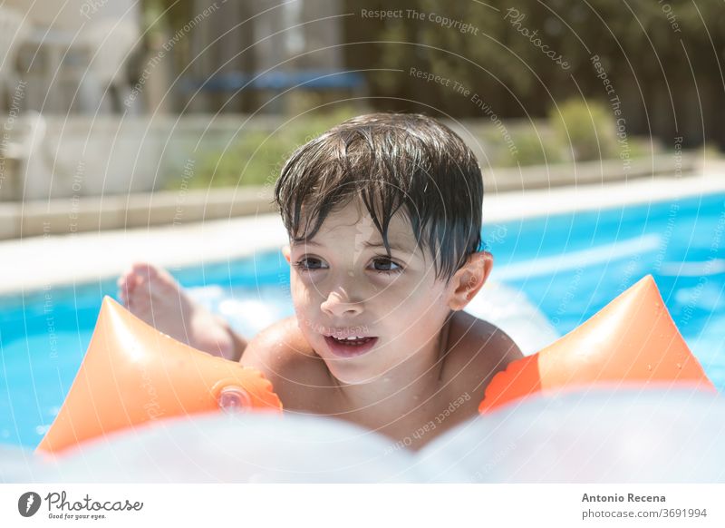 toddler with muffs and float on a mat in a swimming pool above ground pool ahead backyard boy calm caucasian child childhood floatie goggles inflatable kid