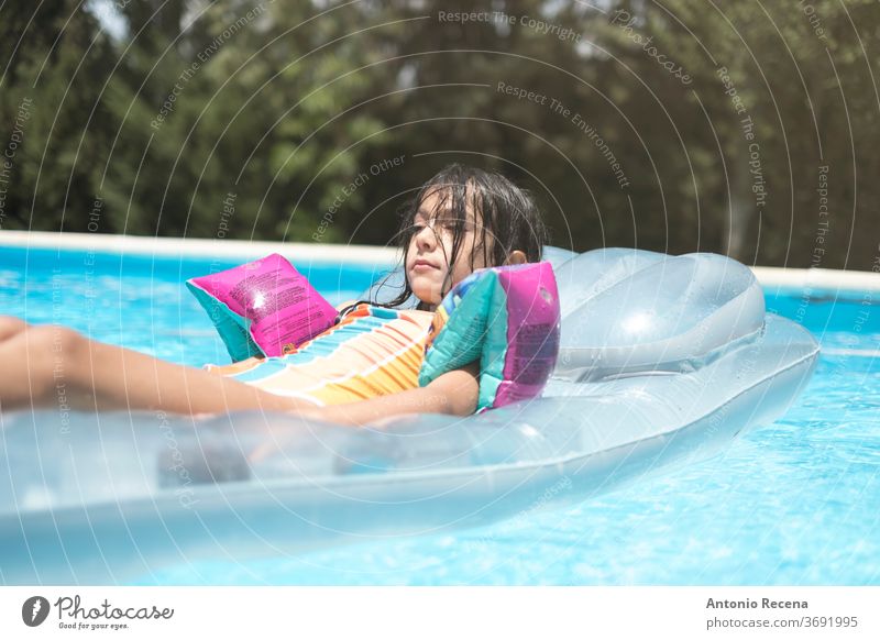 relaxed little girl with muffs on inflatable mat above ground pool ahead backyard calm caucasian child childhood float floatie goggles kid leisure looking male