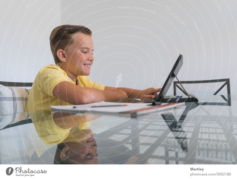 Boy talking with classmate during video call on tablet and discussing homework while sitting at table in modern light room. homeschool indoors child remote