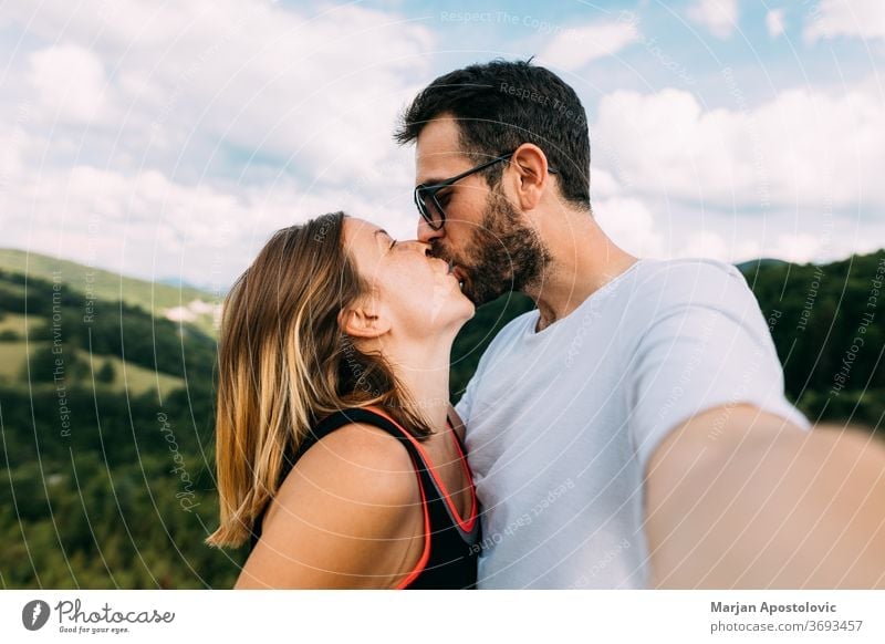 Young couple taking a selfie while kissing in the mountains adult adults adventure affectionate beautiful boyfriend camera casual caucasian cheerful emotional