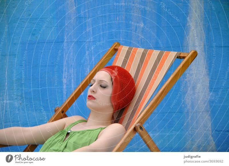 The girl with the beautiful red bathing cap and green swimsuit takes a sunbath in a deck chair. A summer love. Girl Woman Swimwear Bathing cap Swimsuit Summer
