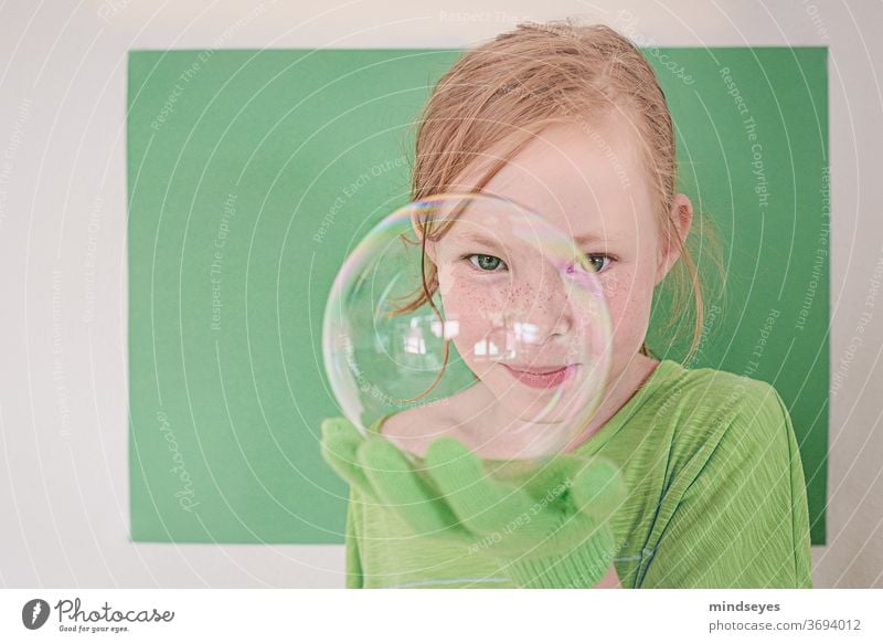 Girl in green looks cheekily through a soap bubble soap bubbles Soap bubble magic Gloves Playing fun Infancy Joy Funny Brash Freckles Child Colour photo