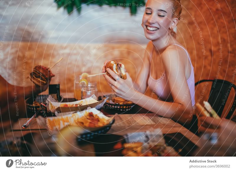 Happy young woman eating burger in cafe having fun fast food cheerful happy friend together hamburger laugh lifestyle friendship meeting communicate female