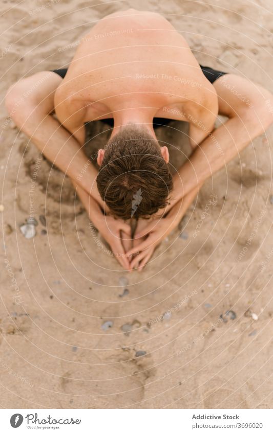 Focused man doing yoga on beach practice sand asana sit bound angle baddha konasana bend forward male yogi slim shirtless healthy lifestyle balance zen posture