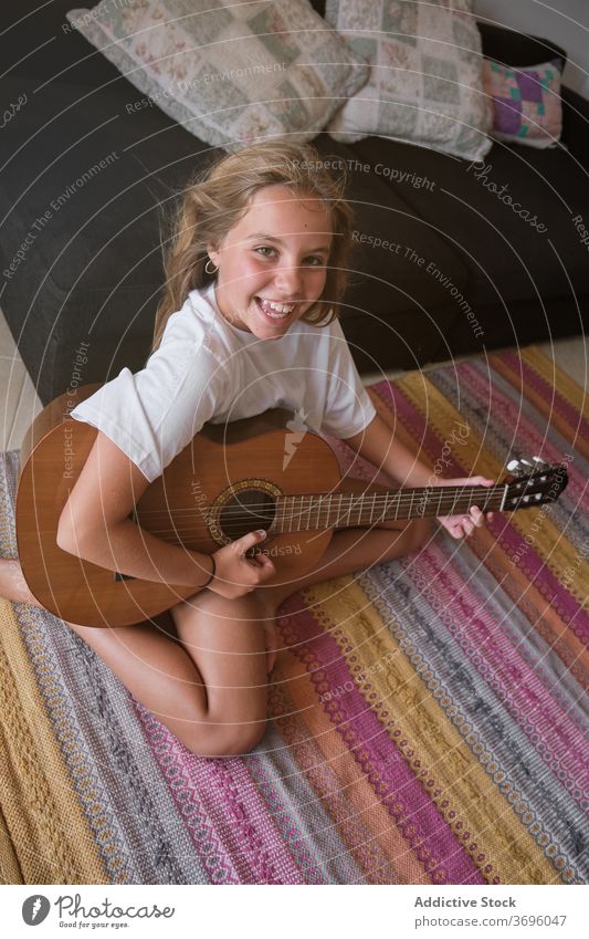 Girl sitting on the floor playing a guitar while is smiling and facing the camera vertical music artist classical learning musician practice room smile string