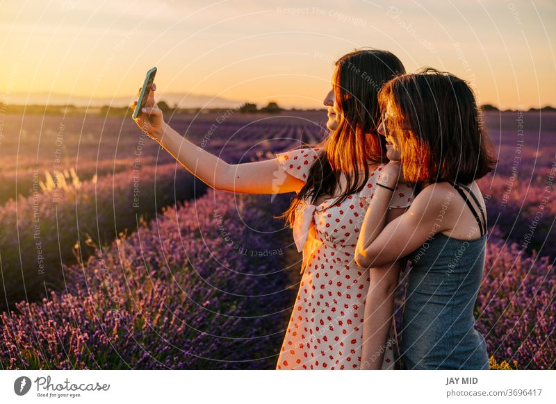 Two friends take photos with their mobile phone in a field of blooming lavenders woman´s two holiday make photos selfie summer vacation blossom enjoy fun play