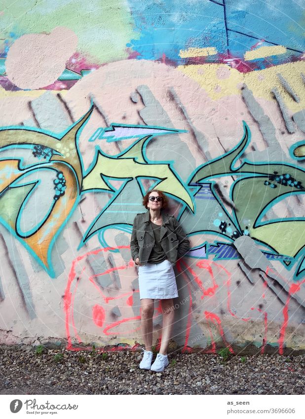 Woman with sunglasses in front of a wall with graffiti Graffiti sneakers Sunglasses lured Red-haired Exterior shot Day Human being Fashion green Khaki