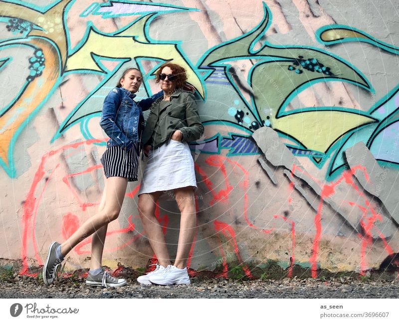 Two women in front of a wall with graffiti Graffiti sneakers Sunglasses lured Red-haired Exterior shot Day Human being Fashion green Khaki variegated Pattern