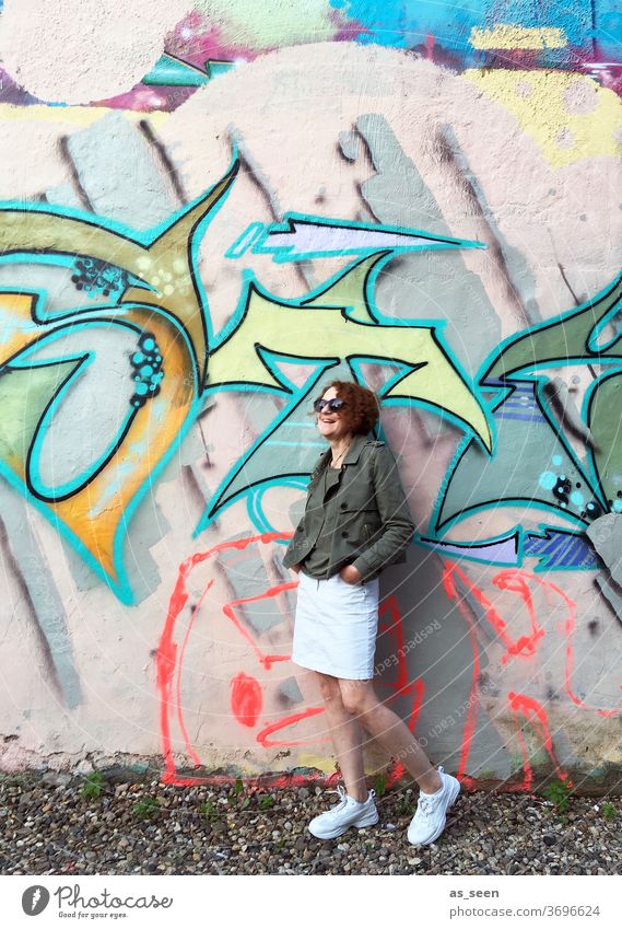 Woman with sunglasses in front of a wall with graffiti Graffiti sneakers Sunglasses lured Red-haired Exterior shot Day Human being Fashion green Khaki