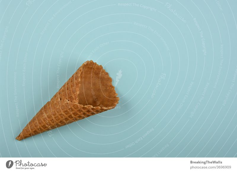 One empty wafer ice cream cone over blue Ice cornet brown closeup table pastel paper elevated top view directly above high angle copy space sweet food