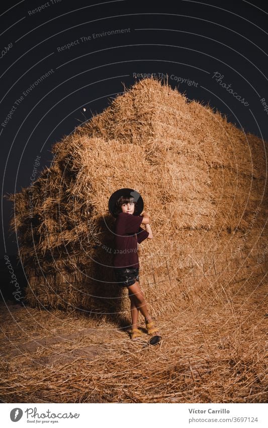 A young boy with a hat playing in the fields of the country side in summer in a straw bale background farmer boy crouching plant autumn kid cute fall plantation