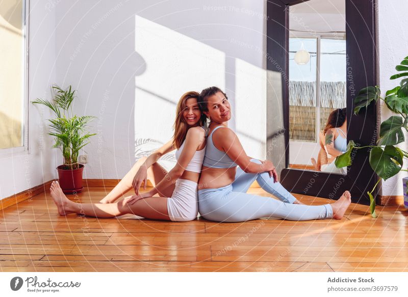 Delighted women doing yoga at home practice together flexible asana rest smile friend sportswear floor healthy wellness sit happy relax wellbeing back to back