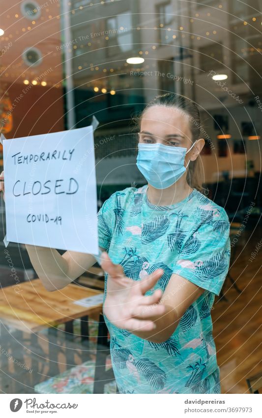 Woman placing coronavirus closure sign owner protective face mask sticking poster closing covid-19 cafe surgical mask quarantine woman temporarily female bar