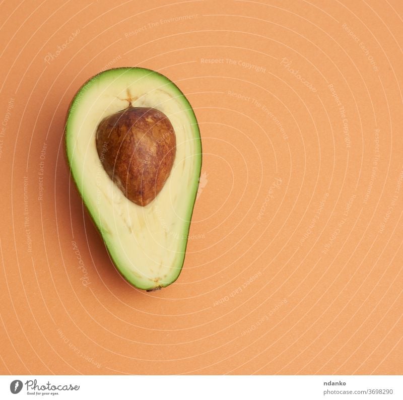 half ripe green avocado with a brown bone on an abstract orange background closeup color creative cut delicious diet dieting eating exotic food fresh freshness