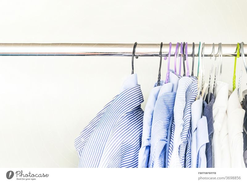 A group of men's shirts of various colors hung with hangers inside a wardrobe hanging dress cotton fabric striped light blue white bar coat hanger adult fashion
