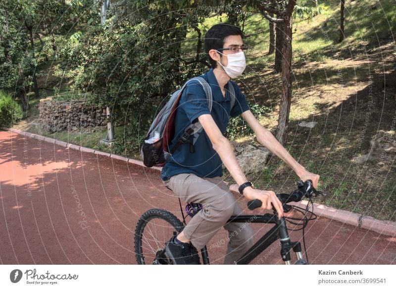 Isolated and masked young male riding a bike at a public park corona coronavirus global epidemic pandemic person man surgical mask bicycle cycling forest