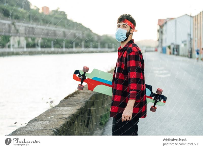 Male hipster in medical mask in city skater longboard promenade man coronavirus walk protect male surgical young summer hobby urban street handsome serious