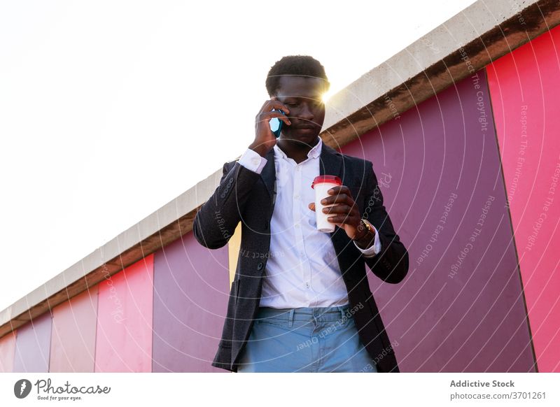 Stylish businessman with coffee talking on smartphone on street urban takeaway serious discuss call young african american black ethnic disposable cup device