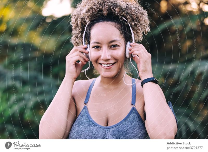 Cheerful sportswoman listening to music with headphones in park sporty happy cheerful fitness enjoy adjust energy young smartphone workout training healthy