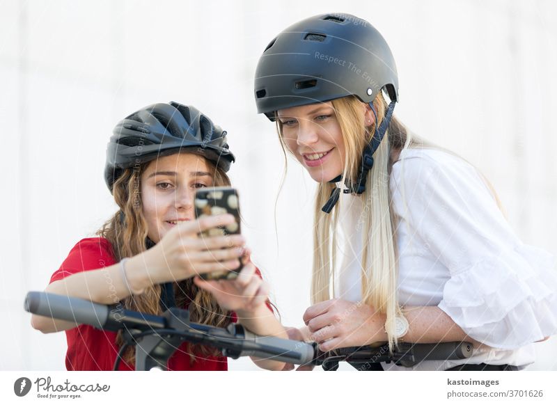 Teenager girls using mobile application to unlock and rent riding public rental electric scooters in urban city environment. Eco-friendly modern public city transport in Ljubljana, Slovenia.