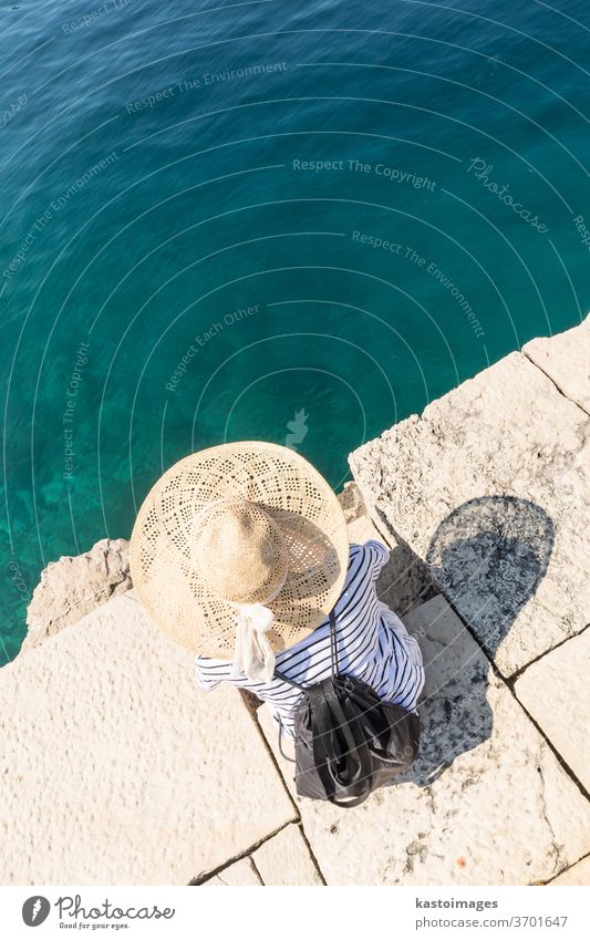 Graphic image of top down view of woman wearing big summer sun hat relaxing on pier by clear turquoise sea. water leisure beauty girl person blue tan body young