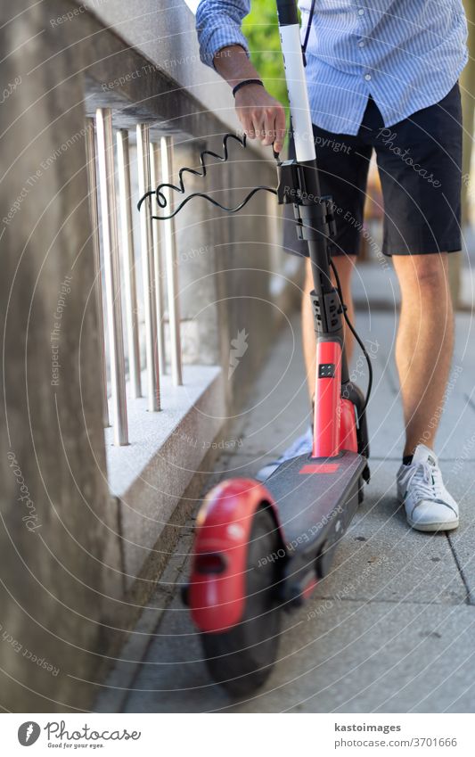 Male user safely parking electric scooter and locking it to a fence. Eco friendly green modern urban mobility concept of sharing transportation with electric scooters for rent in Ljubljana, Slovenia