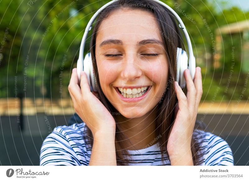 Calm woman listening to music in city headphones enjoy song carefree dreamy satisfied female glass wall building mirror reflection wireless relax happy gadget