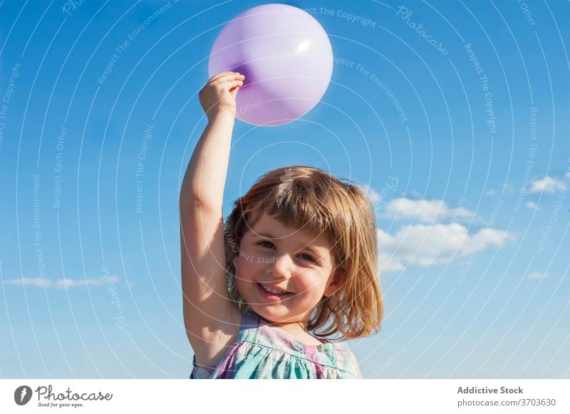 Content girl with balloon in summer child having fun kid toy air balloon joy childhood smile dress cheerful holiday summertime blue sky sunshine bright adorable