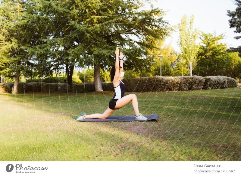 Young brunette woman with a mask exercising and stretching on a mat in the park fit yoga pandemic covid fitness exercise meditation coronavirus sports balance