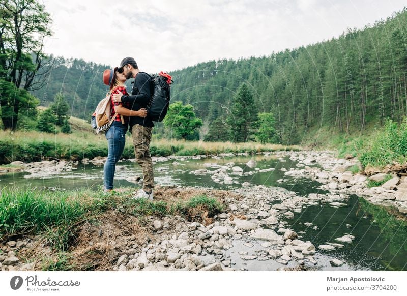 Young couple nature explorers kissing by the river in the mountains adult adventure backpack backpacker casual creek expedition exploration forest happy hike