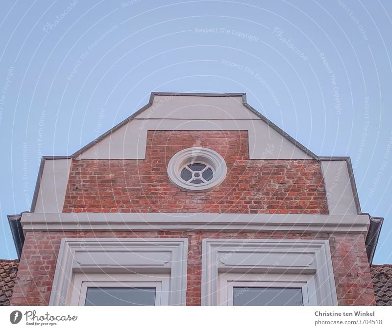 House gable / relay gable with red clinker bricks, white plaster and a round pretty window in front of a light blue sky house gables Gable pediment