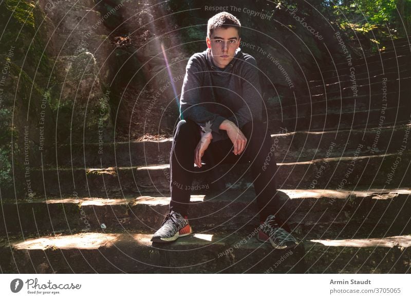 Portrait of a serious young man sitting on a staircase stairs bw cool casual sunlight sunbeam outdoors perspective trendy confident portrait teenager looking