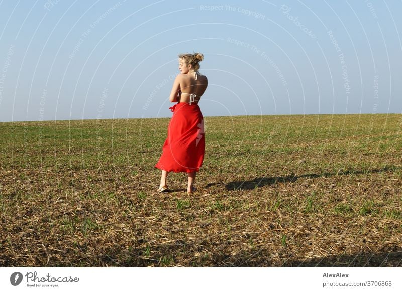 Portrait in back view of a young woman with bikini top and red skirt on a field Light Athletic Feminine Emotions emotionally portrait Central perspective