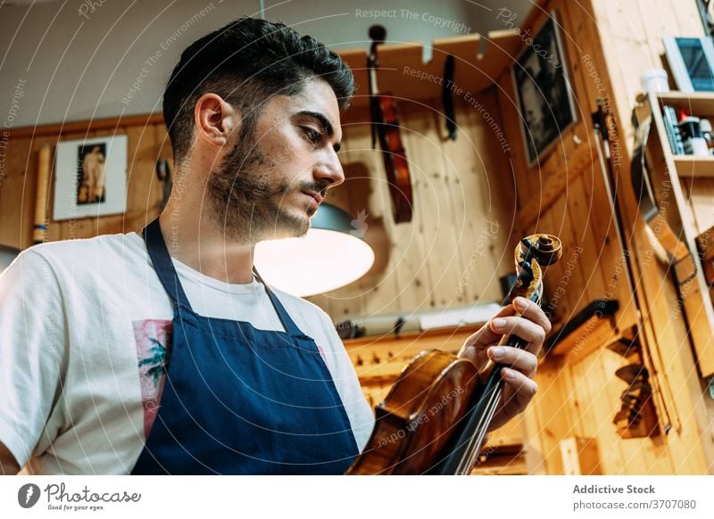 Male master in workshop with violins man repairman instrument music craftsman workbench apron male shiny equipment modern hobby tool focus table professional