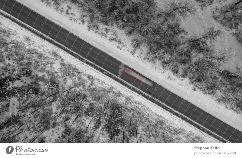 Aerial view on a winter street framed by snow, a car is passing by as a long exposure shot. road diagonal line lights schwaebische alb albstadt living drone
