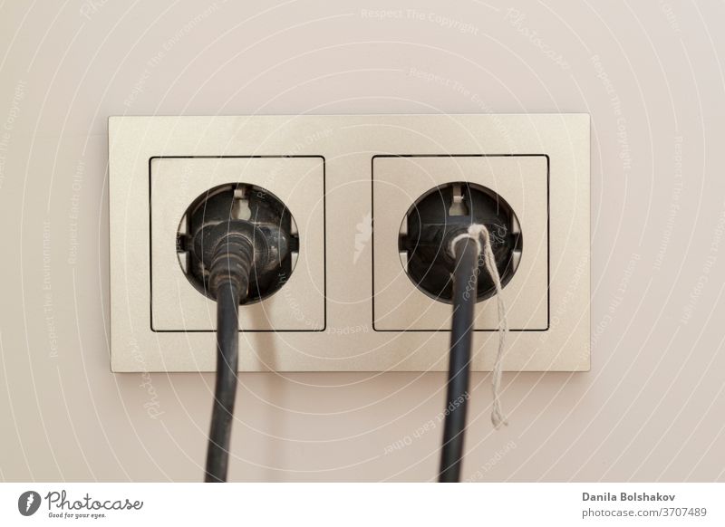 two black plugs are plugged into a double electrical outlet with a frame technical electronics extension cord power supply two pin plug power line power cable