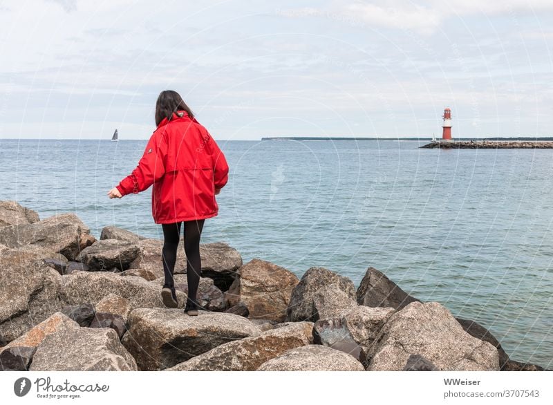 Young girl balances on the big stones of the western pier Young woman Balance Boulders Mole Wetsmole Warnemünde Rostock Lighthouse Baltic Sea Harbour Sky Red