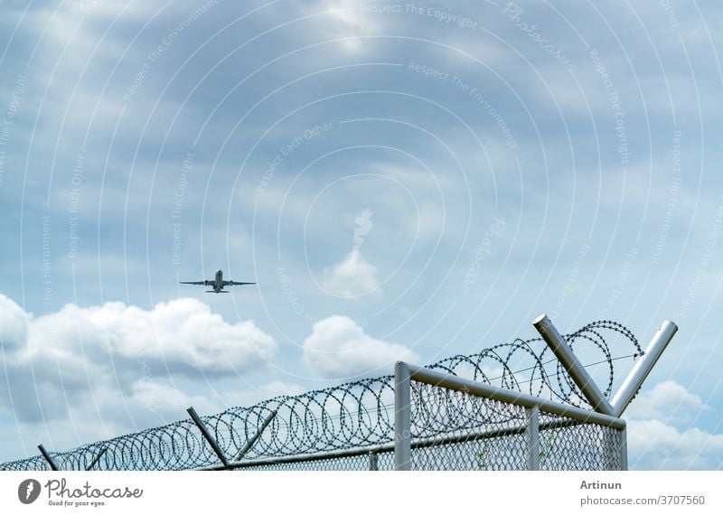 Airplane flying on blue sky and white clouds above metal fence. Aviation business. Commercial plane. Air transportation. Fence for safety and security. Aviation business. Travel by plane.