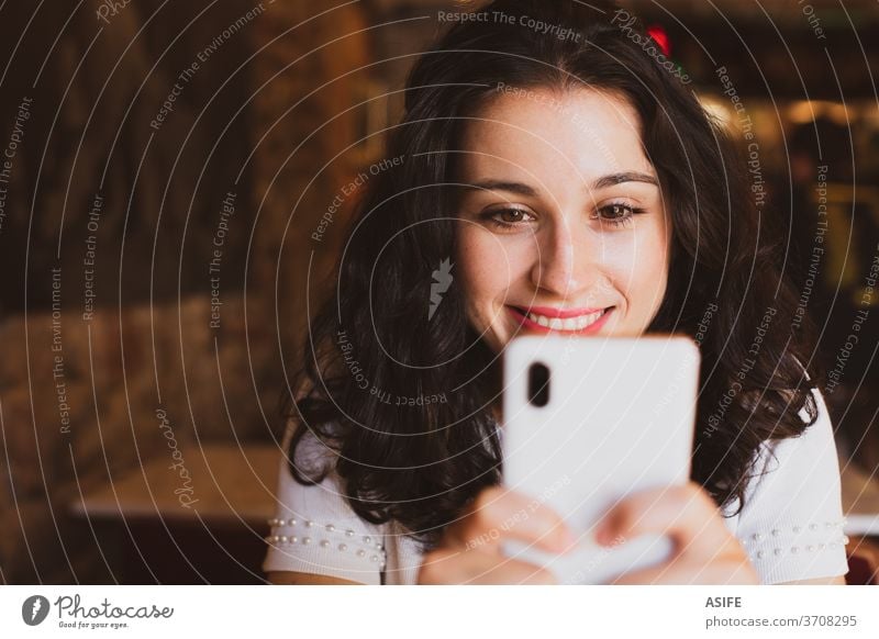 Happy young beautiful woman using her smartphone in a bar girl cafe portrait happy smile person joy people toothy face close up mobile phone smart phone